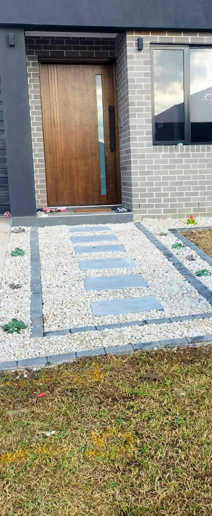 Stepping-stone path of grey pavers set in white pebble, leading to a timber front door