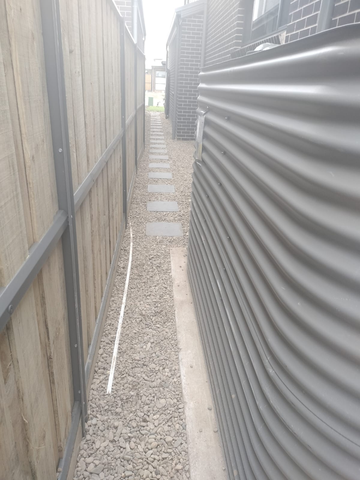 Narrow side passage finished in pebble with stepping stones, beside a rainwater tank